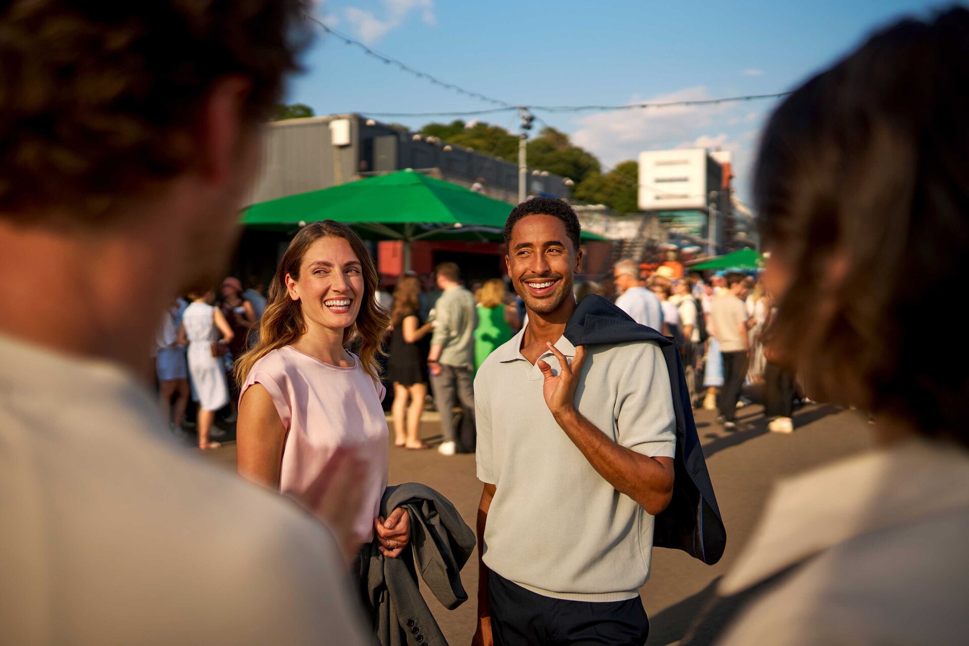 Zwei Personen lächeln und sprechen bei einem belebten Networking-Event bei sonnigem Wetter.