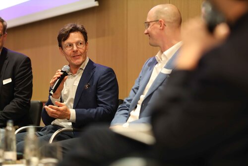 Zwei Männer diskutieren auf einer Bühne, Mikrofon in der Hand. Impressionen der Veranstaltung "Exzellenz durch Kongresse" mit Podiumsdiskussion und Networking.