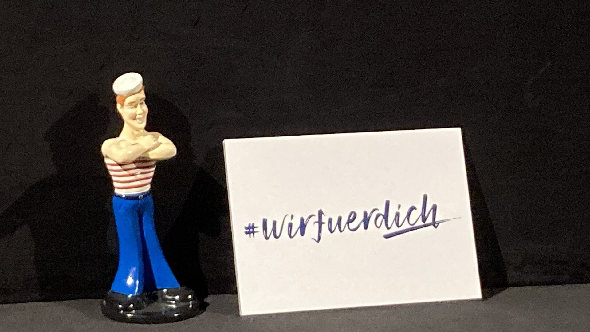 Eine Figur eines Matrosen und eine Karte mit #WIRFUERDICH.