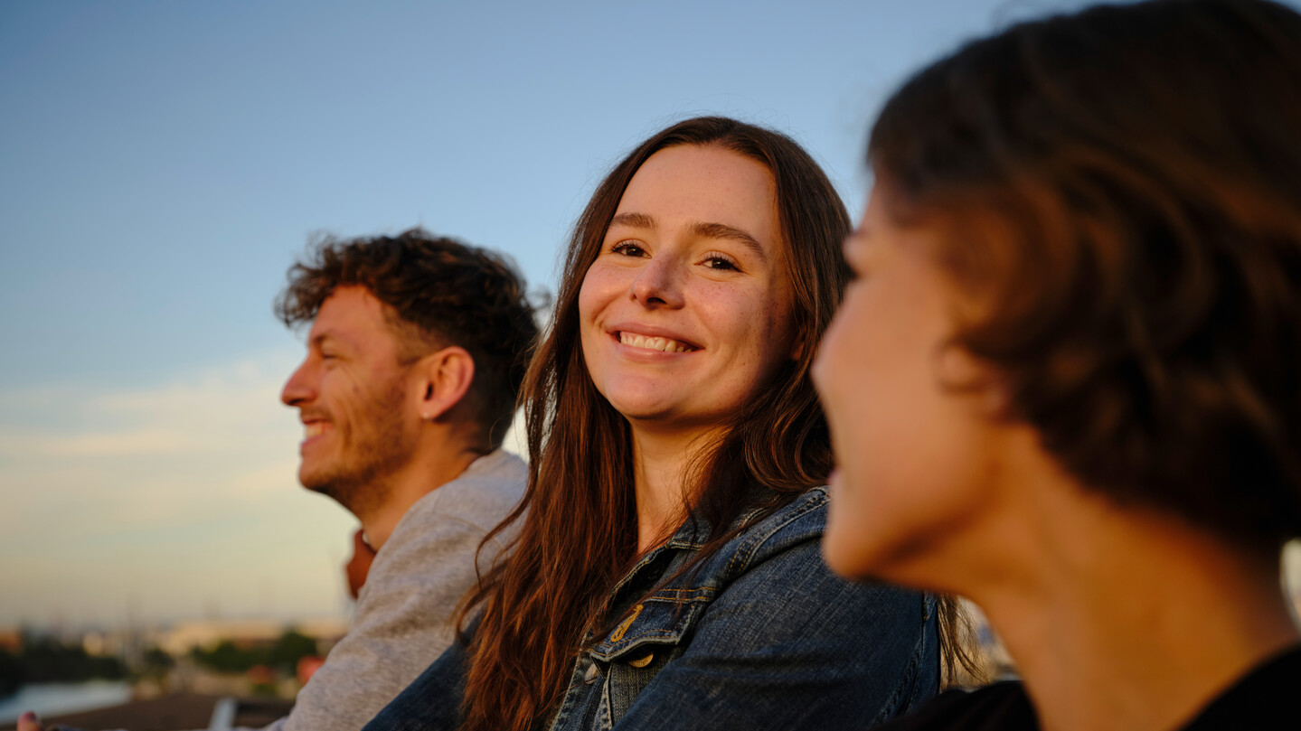 Drei Personen lachen und genießen eine schöne Aussicht bei Sonnenuntergang.